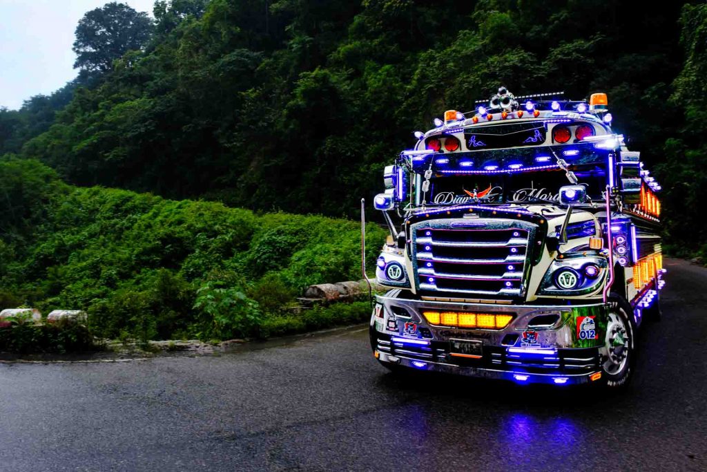 Brightly decorated blue chicken bus driving along green Guatemalan hills.